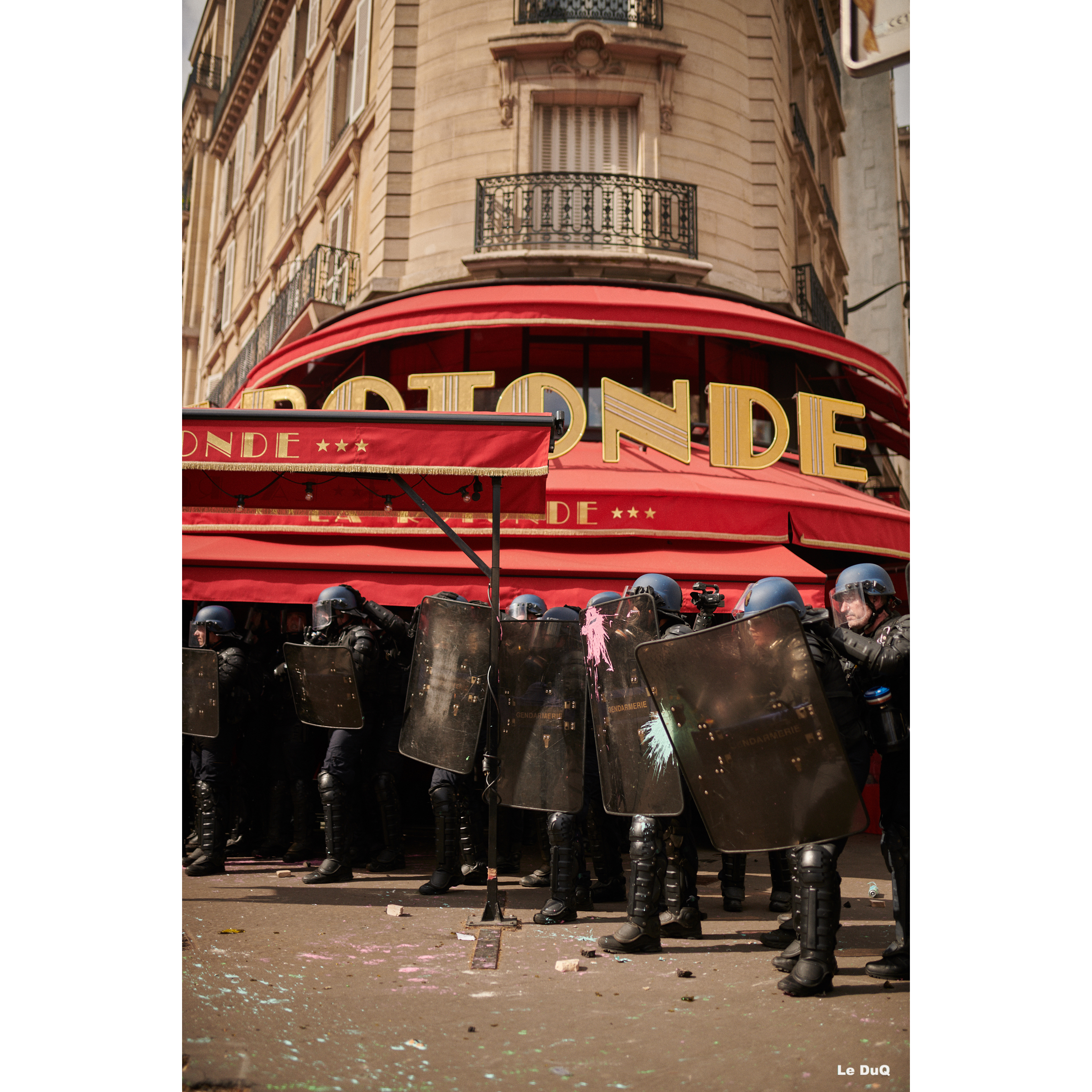 Des CRS défendant la devanture du restaurant La Rotonde se font asperger de bombes de peinture.